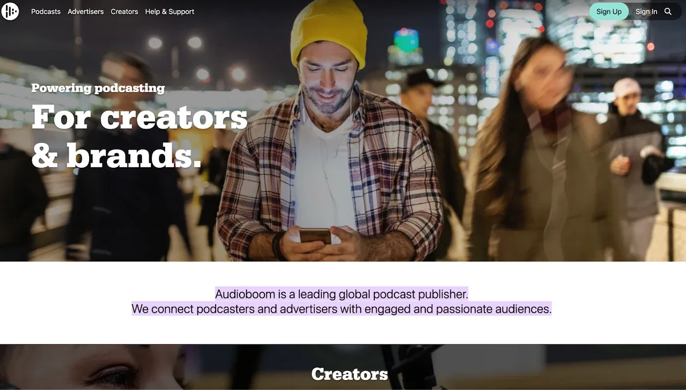 Audioboom homepage headline "Powering podcasting For creators & brands." over a man in a yellow beanie using his phone.